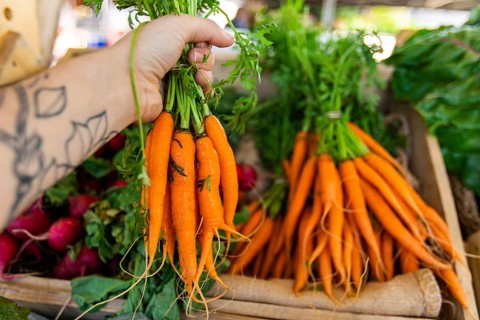 First person perspective as a shopper buys locally produced organic carrots at a market stall