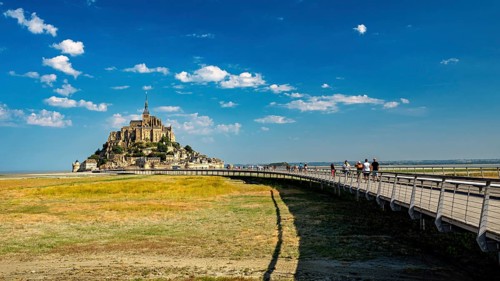 Mont Saint-Michel in summer with a pedestrian bridge in the foreground and blue sky, Mont Saint