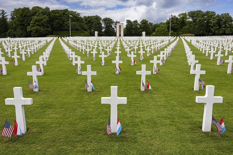 White crosses of an American military cemetery on a green lawn, lined with flags, Luxembourg