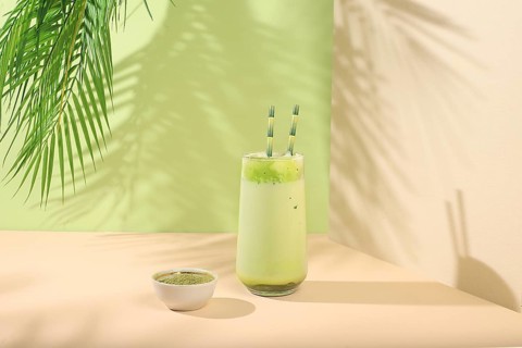 Green tea matcha latte in a glass with bamboo tubes on a modern light background with palm leaves