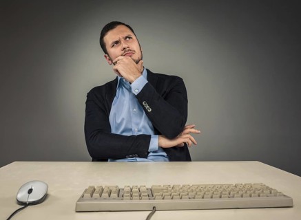 Handsome man in blue shirt and jacket looking up, sitting at a desk near a computer, isolated on