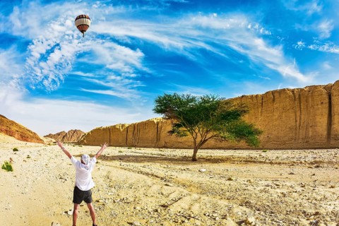 The huge multi-colored balloon flies over desert near the seaside resort of Eilat. The tourist in