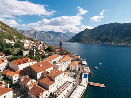 Old houses with red roofs on the shore of the Bay of Kotor with a swimming pool on the promenade.