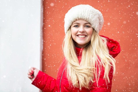 Portrait of a beautiful blonde girl in a warm hat and red jacket and falling snow