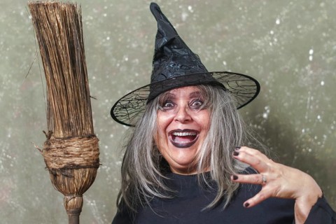 Old witch with white hair and a black hat with an ancient broom in her hands and a terrifying