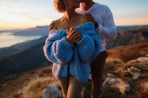 Man hugs a woman in a blue sweater by the shoulders on the background of mountains. Close up.