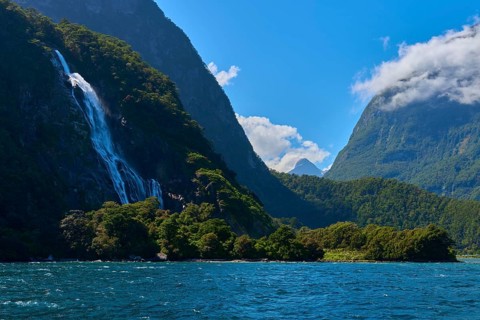 Majestic waterfall flows from forested mountain into the water under a clear blue sky, summer,