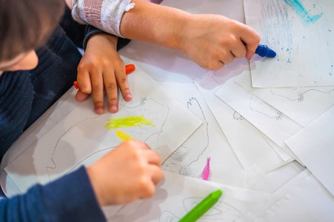 Two kids coloring drawings of animals with wax crayons, developing their creativity and fine motor