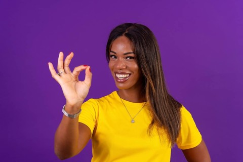 Studio portrait with purple background of an african smiling urban woman gesturing agreement with