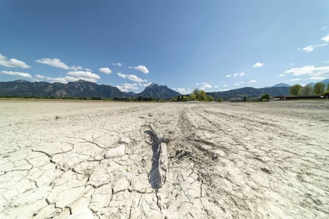 Cracked, dried out ground, waterless Forggensee in spring, behind it Tegelberg massif and Säuling,