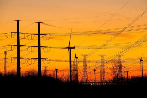 High-voltage electricity pylons, transmission towers and wind turbines at sunset near the Borssele