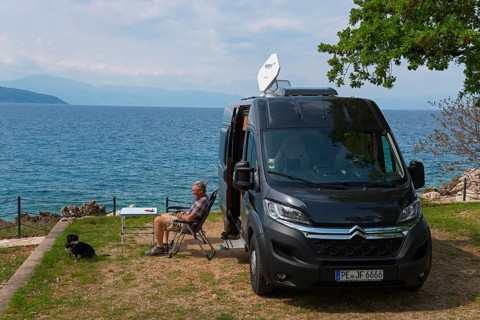 A campsite by the sea, a man sits next to a motorhome and enjoys the view with a dog, Glavotok, Krk