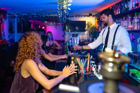 Bartender mixing vibrant cocktails in a trendy nightclub, serving young women at the bustling bar