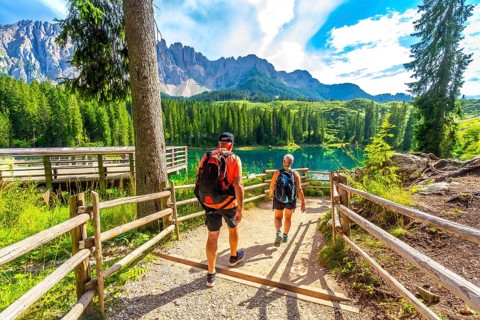 Tourists walking on a path towards the turquoise waters of lake carezza, surrounded by the stunning
