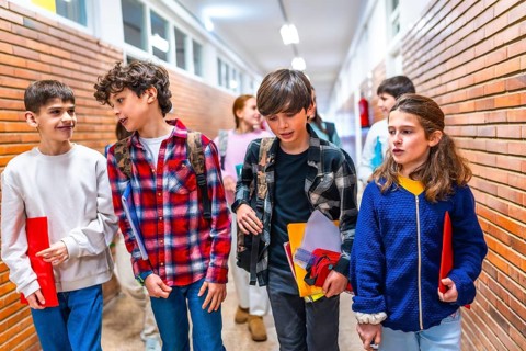 Elementary school students carrying backpacks and notebooks walk and chat together in school