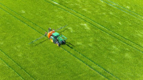 Farmer with tractor working in the field. In early summer, he fertilises the grain for an optimum