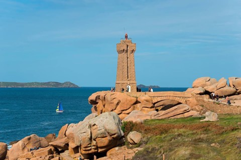 Lighthouse overlooking the rocky coast with sailing boat on the horizon, Phare de Men Ruz,