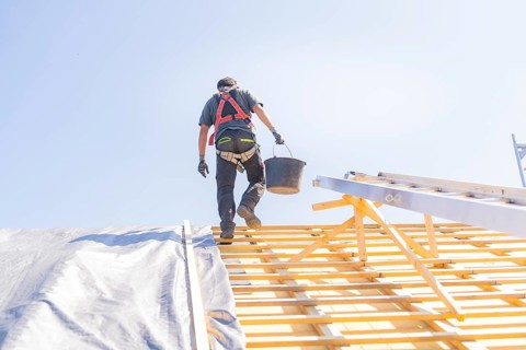 A worker in safety clothing climbs a ladder to work on a roof, in sunny weather, roof renovation,