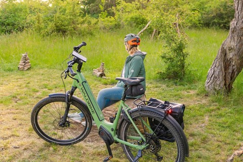 Cyclist with helmet sitting next to a bicycle, surrounded by green nature and trees, e-bike