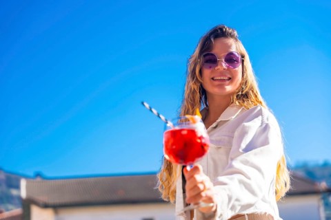 Chic blonde woman toasting with the camera holding a red cocktail in a rooftop in summer