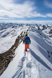 Mountaineer on a narrow mountain ridge in winter, summit of Piz Grialetsch, view of mountain