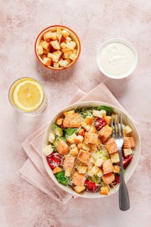 Caesar salad with salmon, with croutons and dressing, in a salad bowl, on a pink table