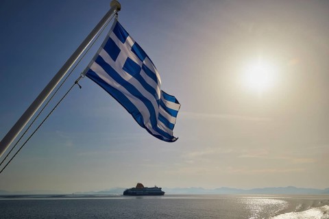 Greek flag waving, with a ship in the background and sunny sky, crossing Rhodes to Symi, ferry,