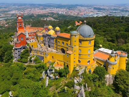 Impressive castle with colourful towers and domed roof on a mountain ridge amidst green trees and