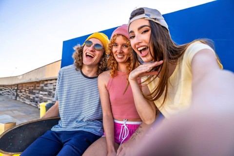 Three joyful skaters enjoying a sunny day, capturing a fun selfie against a vibrant blue wall,