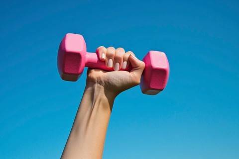 Woman's hand holding pink dumbbell free weight in front of blue sky. Generative Ai, AI generated