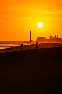 Tourists walking on the maspalomas dunes at sunset, with the maspalomas lighthouse in the