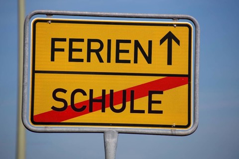 (Photomontage) Symbolic image summer holidays: Town exit sign with text HOLIDAYS and SCHOOL