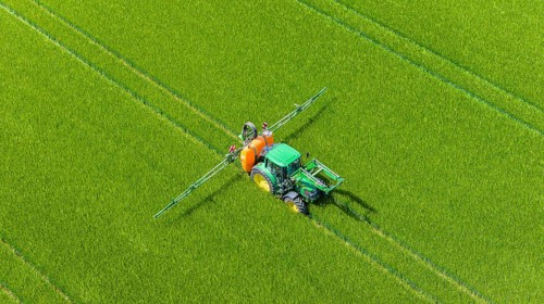 Farmer with tractor working in the field. In early summer, he fertilises the grain for an optimum