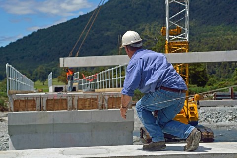 Builders construct a concrete bridge over a small river in Westland, New Zealand