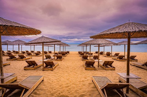 Deserted beach with bamboo umbrellas and sunbeds under a cloudy sky and calm sea, Golden Sands,