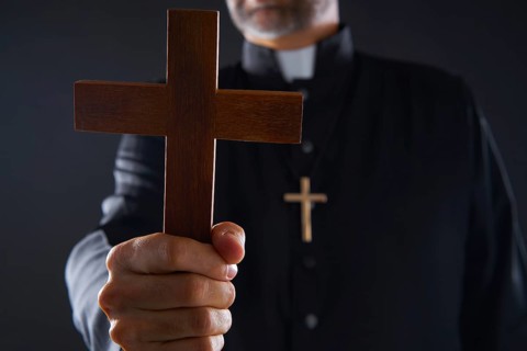 Priest holding cross of wood praying in foreground