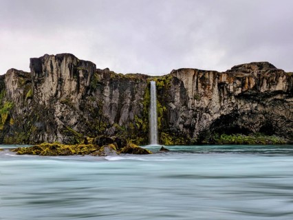 Vibrant waterfall cascading down moss-covered cliffs under a cloudy sky, Icelandic scenery. Iceland