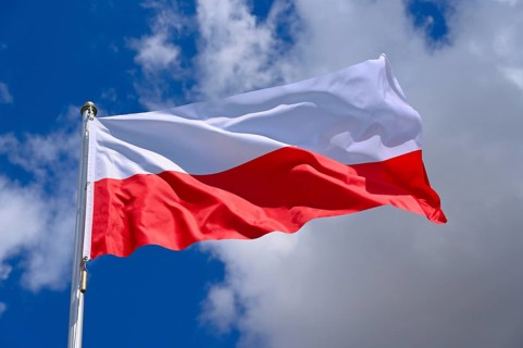 The flag of Poland flutters in the wind in a blue sky with white clouds