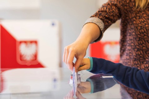 Woman's and kid's hands puting a card with a vote to the ballot box during parliamentary elections.