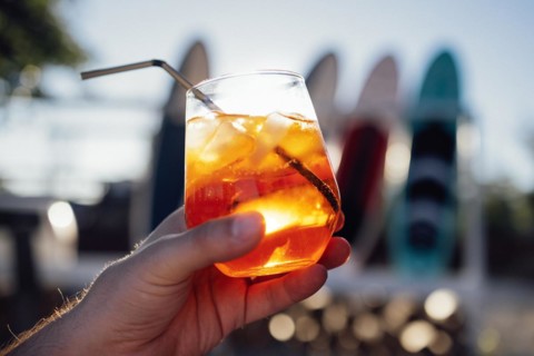 Orange slice and aperol spritz cocktail on a stone against the backdrop of a sandy beach. Man