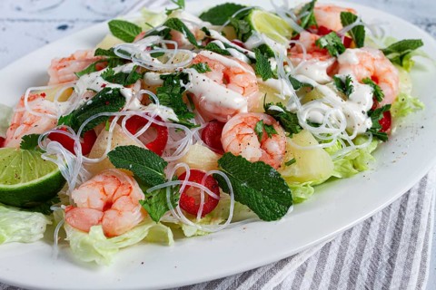 Thai salad with shrimp and rice noodles, pineapple slices, coriander and mint leaves, on a white