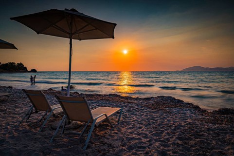 Beach scene with sunset, deckchairs and parasol in warm colours, Mastichari, Kos Island, Greece