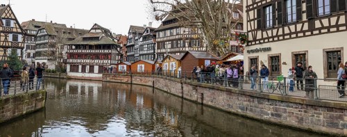 Panoramic photo of the river Ill with strolling tourists, surrounded by half-timbered houses in the