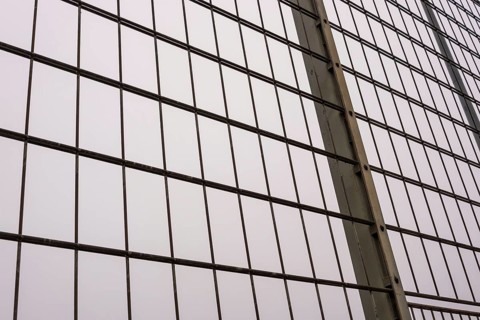 Close-up of a metal mesh wire fence, forming a regular grid pattern against a soft, overcast sky