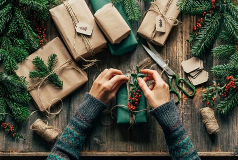 Die Hände einer nicht erkennbaren Frau verpacken Weihnachtsgeschenke auf dem Tisch in einer