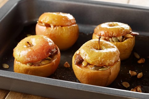 Homemade oven baked apples stuffed with pumpkin seeds and almond nuts in baking pan closeup