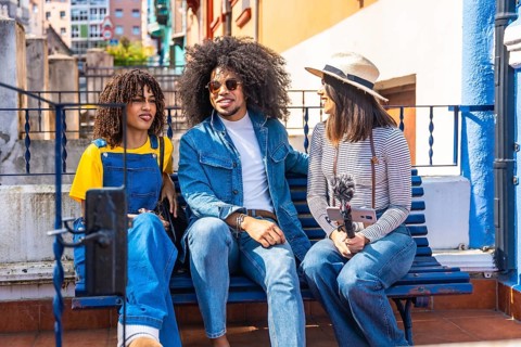 Three young content creators are recording a podcast outdoors, using a smartphone and microphone