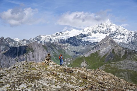 Female mountaineer on hiking trail with cairn, behind glaciated and snow-covered summit of the