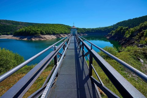 Metal footbridge over a large water reservoir, surrounded by green landscape, summer, Urft dam