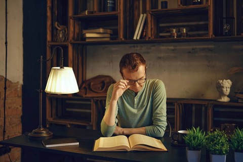 In a serene study space, a thoughtful man sits at a desk, deeply engaged in reading a book. Soft